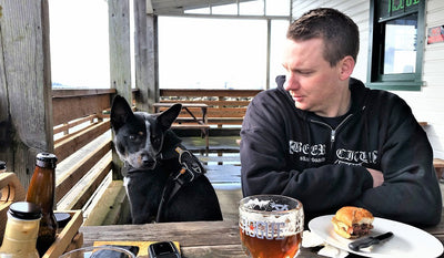 Daniel and his dog Maddie in front range harness sit at table at pub together.