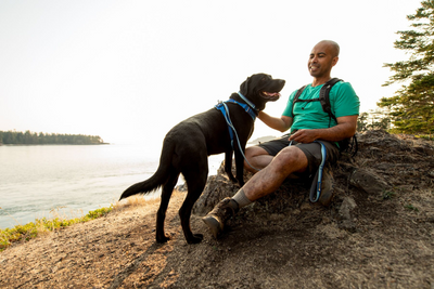 A man and his dog sit on a rock during a hike.