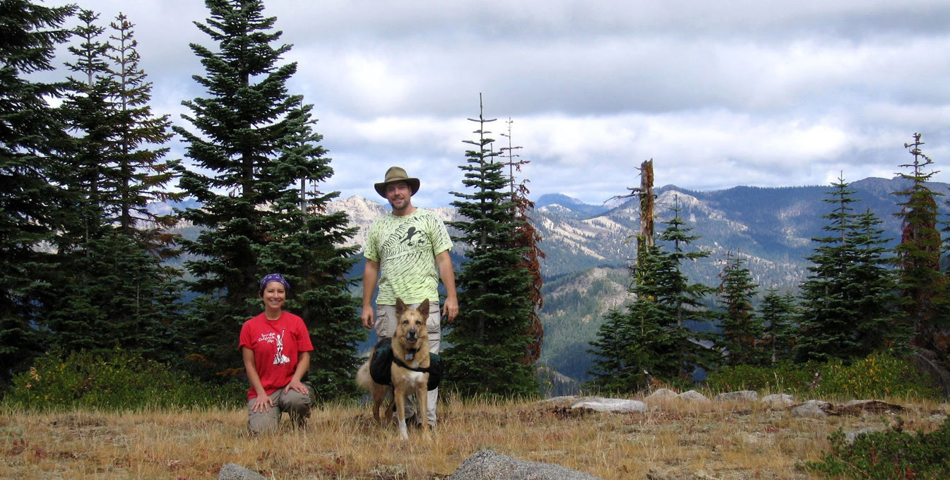 Rene and Jim stand with dog Jerry wearing dog backpack.