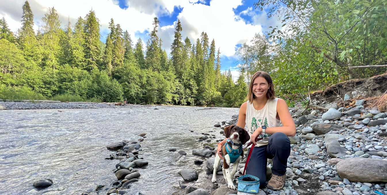 A woman sits by a lake with her puppy. 