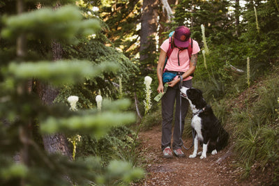Alli pulls a pick up bag out of the Pack Out Bag while her dog RIggins sits at her side on trail.