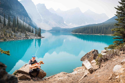 A man stands by a blue lake in Canada with his dog.