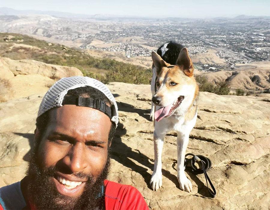 Marcus and Batman take a mid trail run selfie on a hill above a city.