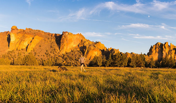 cristina trail running with her dog Lennon across field by Smith Rocks State Park.