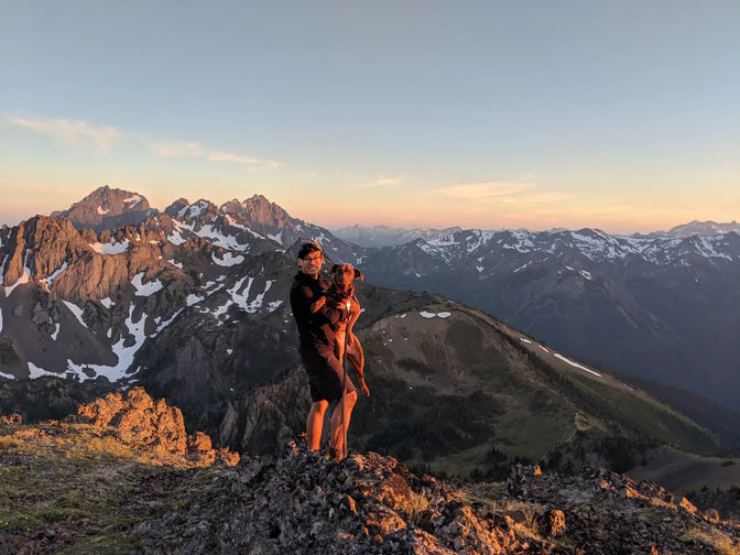 Nathan and Turkey stand on a ridge in the mountains at sunset.
