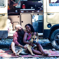 Noami and Dustin sit with Amara on rug outside van.