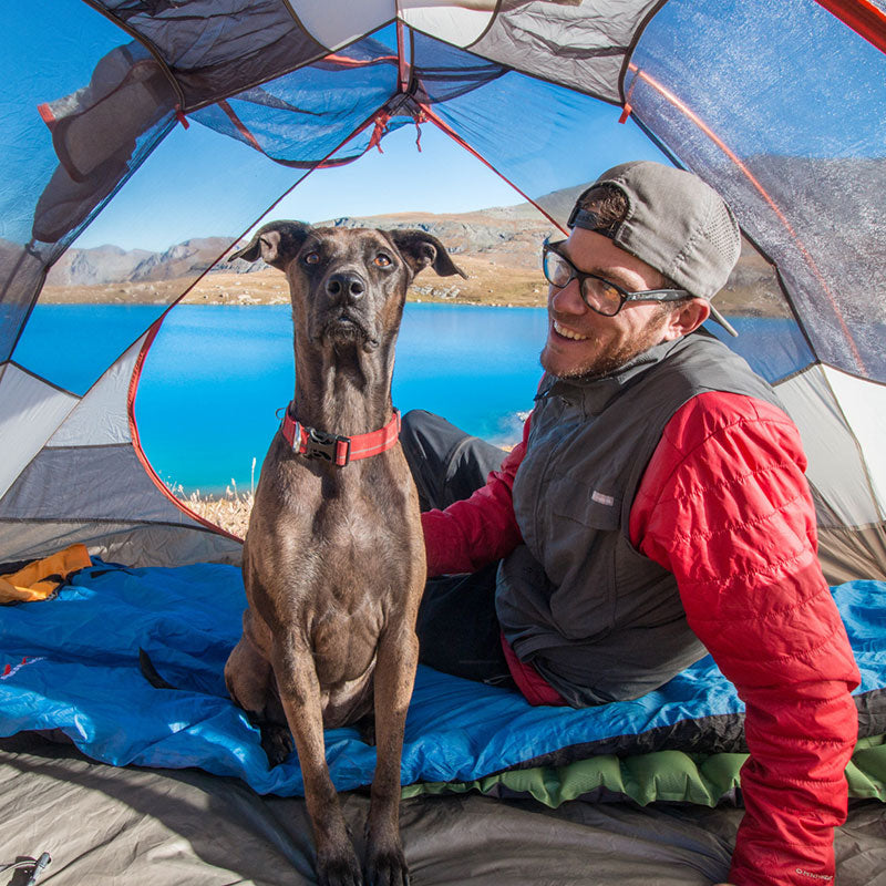 Trevor and Kahlua sit inside a tent next to a lake.