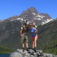 Alicia and her partner with their two dogs on their back standing with mountains in background.